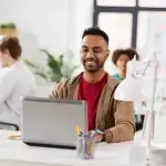 Gezonde werkplek - jongeman zit lachend op kantoor