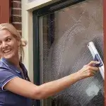 Huishoudelijke hulp - Dame brengt een kopje koffie naar de huishoudelijke hulp die de ramen aan het lappen is. 