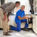 De klusjesman van de klussendienst toont aan een man hoe hij de magnetron in zijn keuken heeft gerepareerd.