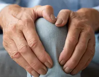 Artrose - twee handen pakken pijnlijke knie vast