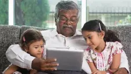 Digitale vaardigheden - opa met tablet en twee kleindochters op de bank