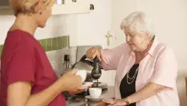 langer thuis wonen - oudere dame maakt thee bij aanrecht samen met jonge dame