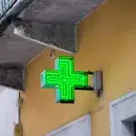 Een groen kruis hangt aan de gevel van een apotheek in het buitenland
