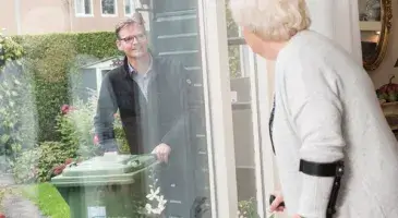 Zorg en hulp thuis - Man met kliko kijkt door raam naar oudere vrouw met krukken