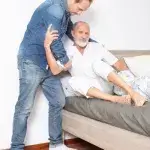Jonge man helpt oudere man bij uit het bed stappen