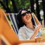 Vrouw met zonnebril op, geniet in de zon van een zomers drankje.