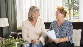 mantelzorg - jongere en oudere dame zitten lachend op bank met papieren