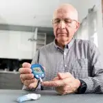 diabetes - senior man test aan tafel zijn suiker met hulp van een apparaatje