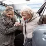 Mantelzorg - Vrouw helpt oudere vrouw bij uitstappen uit de auto