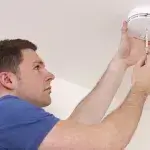 Koolmonoxidevergiftiging voorkomen - man monteert koolmonoxidemelder aan plafond