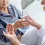 Hand met medicijnen, andere hand reikt glas water aan