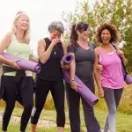 Vier lachende dames wandelen, met yogamat onder de arm