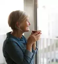 Persoonsalarm Smart - vrouw met kop thee/koffie in de hand kijkt uit het raam
