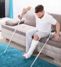 Loophulpmiddelen - man met gebroken been en krukken richt zich op van bank