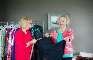 Twee dames bekijken kleding van de kledingservice aan huis bij een lid van de ledenvereniging thuis.