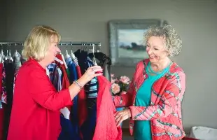 Twee dames bekijken kleding van de kledingservice aan huis bij een lid van de ledenvereniging thuis.