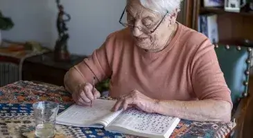 Zorgeloos thuis - oudere dame zit aan tafel en maakt een puzzel