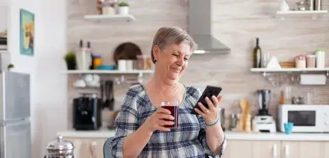 Mevrouw kijkt lachend op haar mobiele telefooon met een kop koffie in de hand