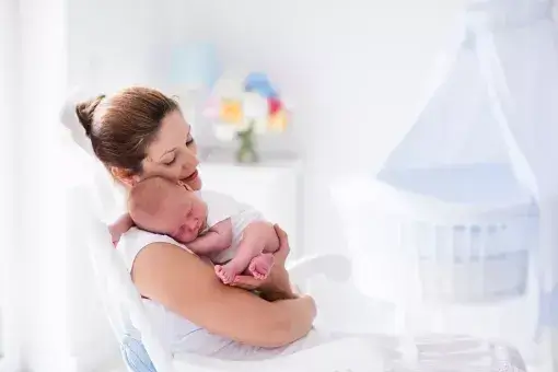 Moeder houdt haar pasgeboren baby op de arm, in de kinderkamer.