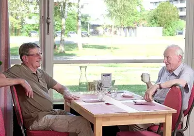 Twee oudere mannen zitten aan een tafel bij het raam